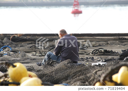 A man who cares for fishing nets spread on the quay 71819404