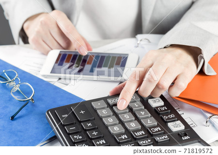 Finance. Female hand with money stack and calculator on financial graphs on desk 71819572