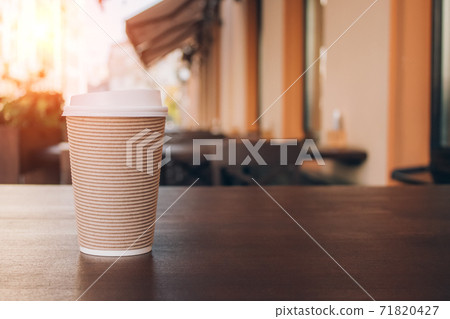 Mockup image of paper cup of coffee take-away, standing on wooden table with blurred cafe behind as background with copyspace. Coffee to go in recyclable paper cup Mockup image of paper cup of coffee take-away, standing on wooden table with blurred cafe behind as background with copyspace. Coffee to go in recyclable paper cup 71820427