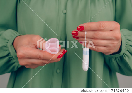 Close up of woman hand with perfect manicure, holding different types of feminine hygiene products - pink menstrual cup and tampons. Women health and hygiene concept, alternative hygiene products Close up of woman hand with perfect manicure, holding different types of feminine hygiene products - pink menstrual cup and tampons. Women health and hygiene concept, alternative hygiene products 71820430