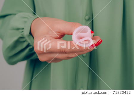 Close up of woman hand with perfect manicure, holding pink menstrual cup - showing how to use, c form. Women health and hygiene concept, alternative hygiene products Close up of woman hand with perfect manicure, holding pink menstrual cup - showing how to use, c form. Women health and hygiene concept, alternative hygiene products 71820432