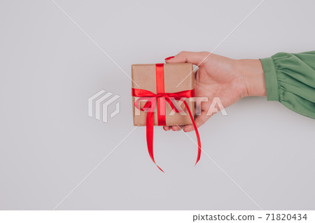 Woman's hand holding present box decorated with red bow . Christmas holidays, New Year or birthday celebration concept. Preparing family gifts for Christmas Woman's hand holding present box decorated with red bow . Christmas holidays, New Year or birthday celebration concept. Preparing family gifts for Christmas 71820434