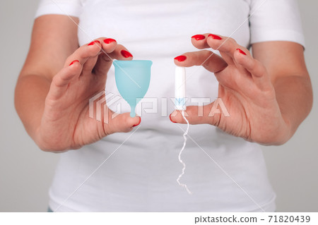 Woman's hand with perfect manicure, holding different types of feminine hygiene products - blue menstrual cup and tampon. Women health and hygiene concept, alternative hygiene products Woman's hand with perfect manicure, holding different types of feminine hygiene products - blue menstrual cup and tampon. Women health and hygiene concept, alternative hygiene products 71820439