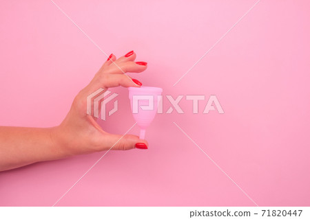 Close up of woman hand with perfect manicure, holding pink menstrual cup over pink background with copy space for text. Women health and hygiene concept, alternative hygiene products Close up of woman hand with perfect manicure, holding pink menstrual cup over pink background with copy space for text. Women health and hygiene concept, alternative hygiene products 71820447