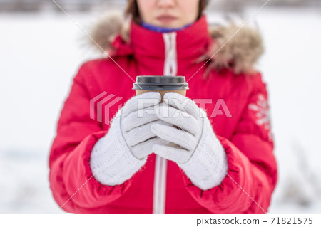 A young woman in winter holds a glass of hot coffee or tea 71821575
