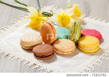 Sweet macarons cakes of different color on silk napkin with bouquet of yellow daffodils 71822782