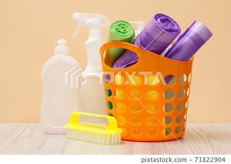 Bottles of dishwashing liquid, basket with garbage bags and brush on wooden desk. 71822904