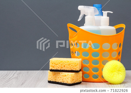 Bottles of dishwashing liquid in a basket and sponges on gray background. 71822926