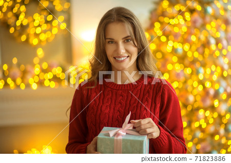 Dark-haired young woman standing with a present in her hands Dark-haired young woman standing with a present in her hands 71823886