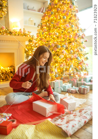 Dark-haired young woman packing christmas gifts and looking excited Dark-haired young woman packing christmas gifts and looking excited 71823929