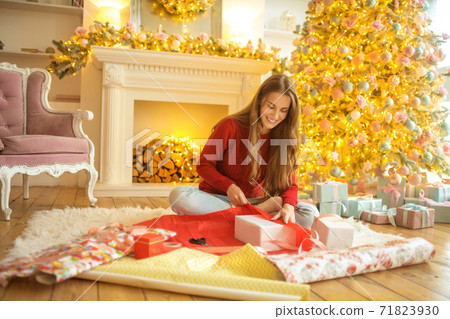 Dark-haired young woman packing christmas gifts and looking excited Dark-haired young woman packing christmas gifts and looking excited 71823930