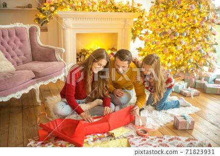 Young family sitting on the floor and packing new year gifts Young family sitting on the floor and packing new year gifts 71823931