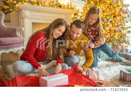 Young family sitting on the floor and packing new year gifts Young family sitting on the floor and packing new year gifts 71823932