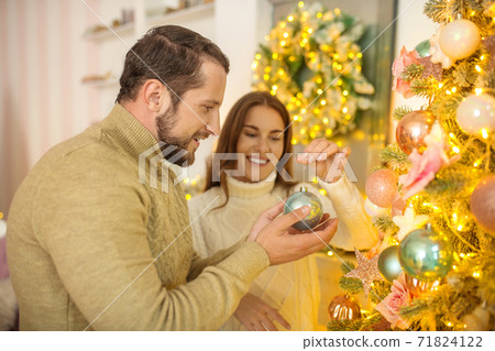 Young happy couple putting christmas bals on a christmas tree Young happy couple putting christmas bals on a christmas tree 71824122