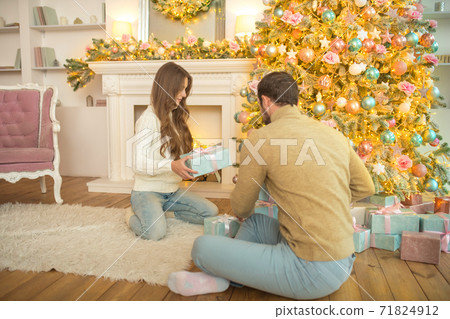 Young happy couple sitting near christmas tree and exchanging the gifts Young happy couple sitting near christmas tree and exchanging the gifts 71824912