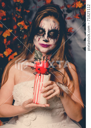 Woman with halloween makeup in wedding dress holds a blood apple 71825112