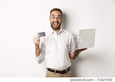 Online shopping. Handsome man showing credit card and using laptop to order in internet, standing over white background 71825450
