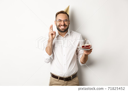 Holidays and celebration. Happy man making wish on birthday cake, cross fingers and smiling excited, having b-day party, white background Holidays and celebration. Happy man making wish on birthday cake, cross fingers and smiling excited, having b-day party, white background 71825452
