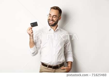 Handsome businessman showing his credit card, looking satisfied, standing over white background Handsome businessman showing his credit card, looking satisfied, standing over white background 71825460