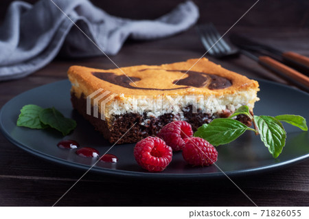 A piece of double-layer cake on a plate of chocolate brownies and curd cheesecake with raspberries. Dark background copy space 71826055