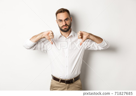 Displeased businessman in glasses showing thumbs down, dislike and disapprove, standing over white background 71827685