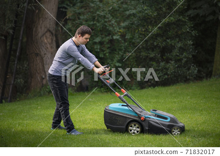 Down syndrome adult man mowing lawn outdoors in backyard, helping with housework concept. 71832017