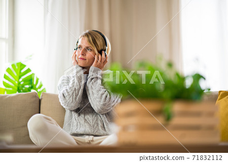 Portrait of woman with headphones relaxing indoors at home, mental health care concept. 71832112