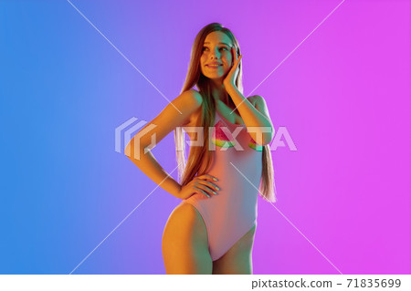 Beautiful seductive girl in fashionable pink swimsuit on bright gradient purple-blue background in neon light Beautiful seductive girl in fashionable pink swimsuit on bright gradient purple-blue background in neon light 71835699