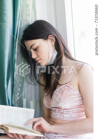 Lonely female isolated at home in protective medical mask on her face looking at window Lonely female isolated at home in protective medical mask on her face looking at window 71838660