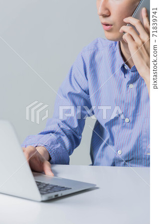 一個年輕人在使用計算機時打與智能手機的電話 一個年輕人在使用計算機時打與智能手機的電話 71839741