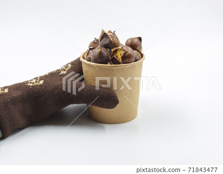 A mittened hand holds a paper Cup of roasted chestnuts. Isolate on a white background, horizontally with space A mittened hand holds a paper Cup of roasted chestnuts. Isolate on a white background, horizontally with space 71843477