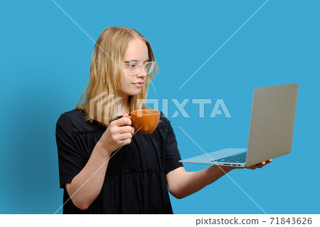 Young cheerful caucasian girl is holding a cup and looking at the Young cheerful caucasian girl is holding a cup and looking at the 71843626