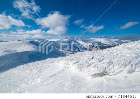 Snow and wind formed ice formations covered winter mountain plateau, tops with snow cornices in far. Magnificent sunny day on picturesque beautiful alpine ridge. 71844615
