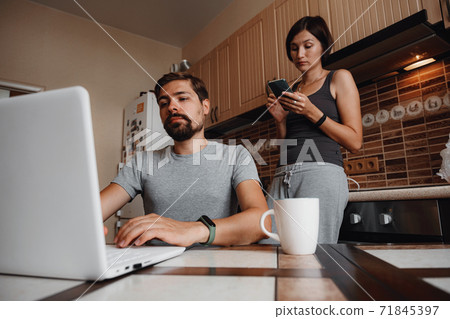 Couple at kitchen, reading news and using laptop. Couple at kitchen, reading news and using laptop. 71845397