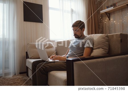Pensive bearded man sitting on sofa work at laptop Pensive bearded man sitting on sofa work at laptop 71845398