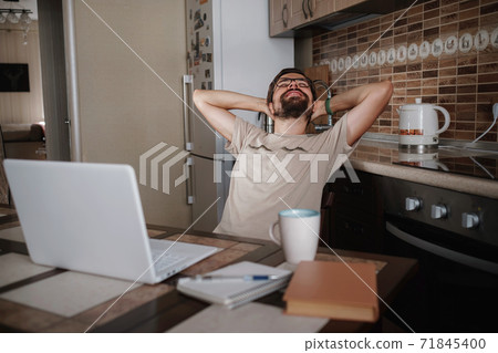 Smiling hipster freelancer holding hands behind head sitting at office desk behind laptop. Smiling hipster freelancer holding hands behind head sitting at office desk behind laptop. 71845400