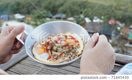 A woman's hand holding a food tray. In the tray is a pan-fried egg dish in the morning winter season. 71845430