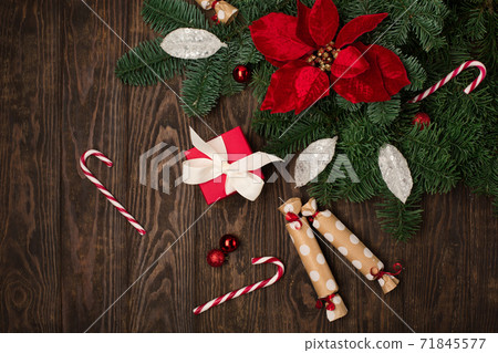 Holiday card - red flower poinsettia, Christmas decorations, gift boxes and candy canes on dark wooden background. 71845577