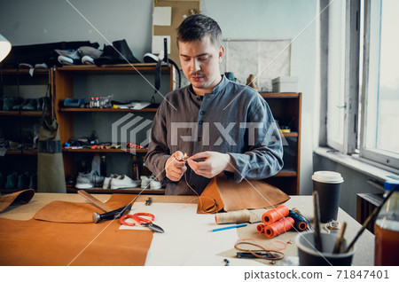 Portrait of a professional shoemaker in the interior of a shoemaker's workshop making a bag made of genuine leather 71847401