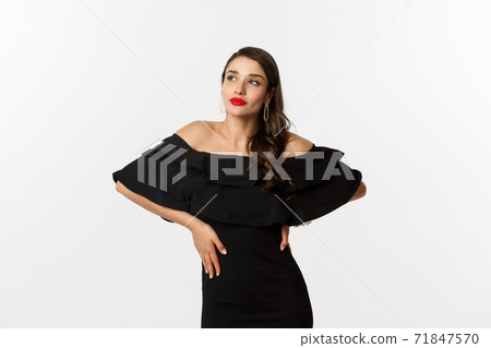 Fashion and beauty. Stylish modern woman in black dress, makeup and red lips, posing over white background self-assured, standing over white background 71847570