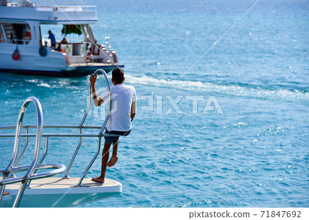 Teenager sits on the edge of a yacht at sea 71847692