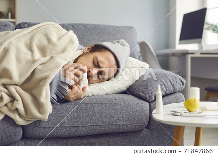 Close up of a sick man with a runny nose with a napkin in his hands lying on the couch. Close up of a sick man with a runny nose with a napkin in his hands lying on the couch. 71847866