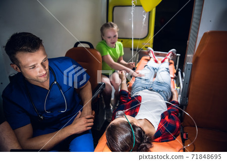 A paramedic and a sad little girl sitting beside a young woman lying on a stretcher in an ambulance A paramedic and a sad little girl sitting beside a young woman lying on a stretcher in an ambulance 71848695