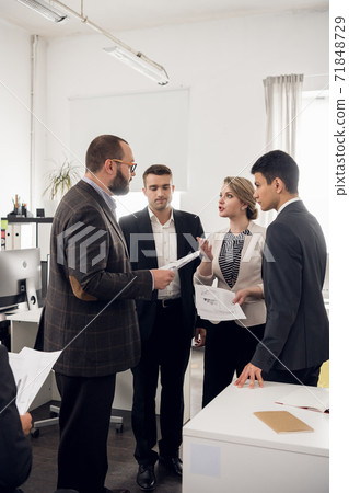 The Director of the company in a jacket gives instructions and tasks to young colleagues in the office of a trading company. 71848729