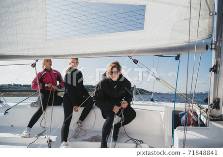 A young guy and two pretty girls set off from the pier on a white sailing yacht for a weekend trip on the lake 71848841