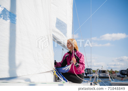 A young athlete in a pink jacket, conducts training on equipping a single-masted sports yacht on the river. 71848849