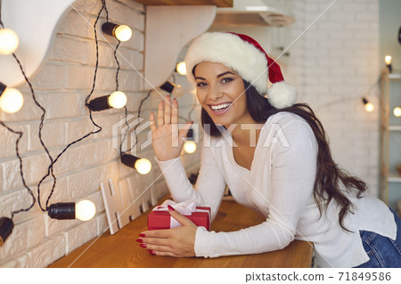 Friendly woman waves his hand in front of the webcam greeting his friends on a video call. Friendly woman waves his hand in front of the webcam greeting his friends on a video call. 71849586