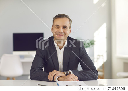 Young smiling businessman sitting and looking at camera during online videocall in office 71849806