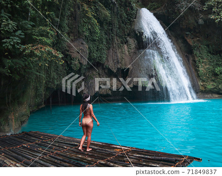 Fit woman alone on the bamboo raft in front of the waterfall with turquoise water in Kawasan Falls in Cebu Island, Philippines 71849837