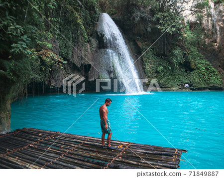 Fit man alone on the bamboo raft in front of the waterfall with turquoise water in Kawasan Falls in Cebu Island, Philippines 71849887
